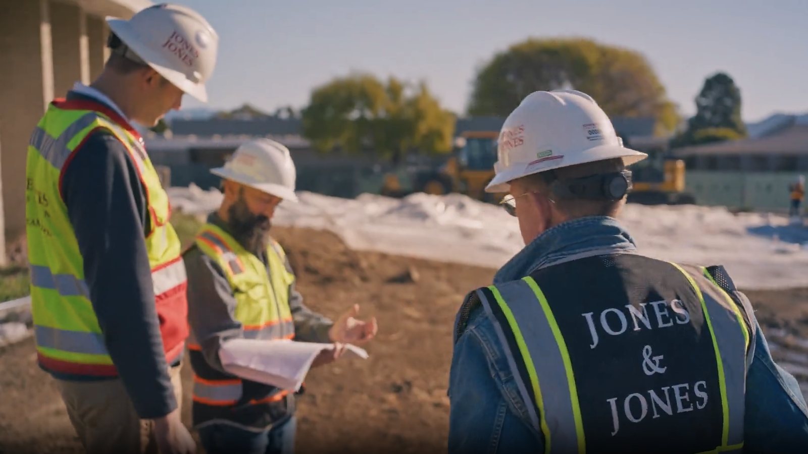 Three men in hard hats and high visibility vests looking over plans on a construction site