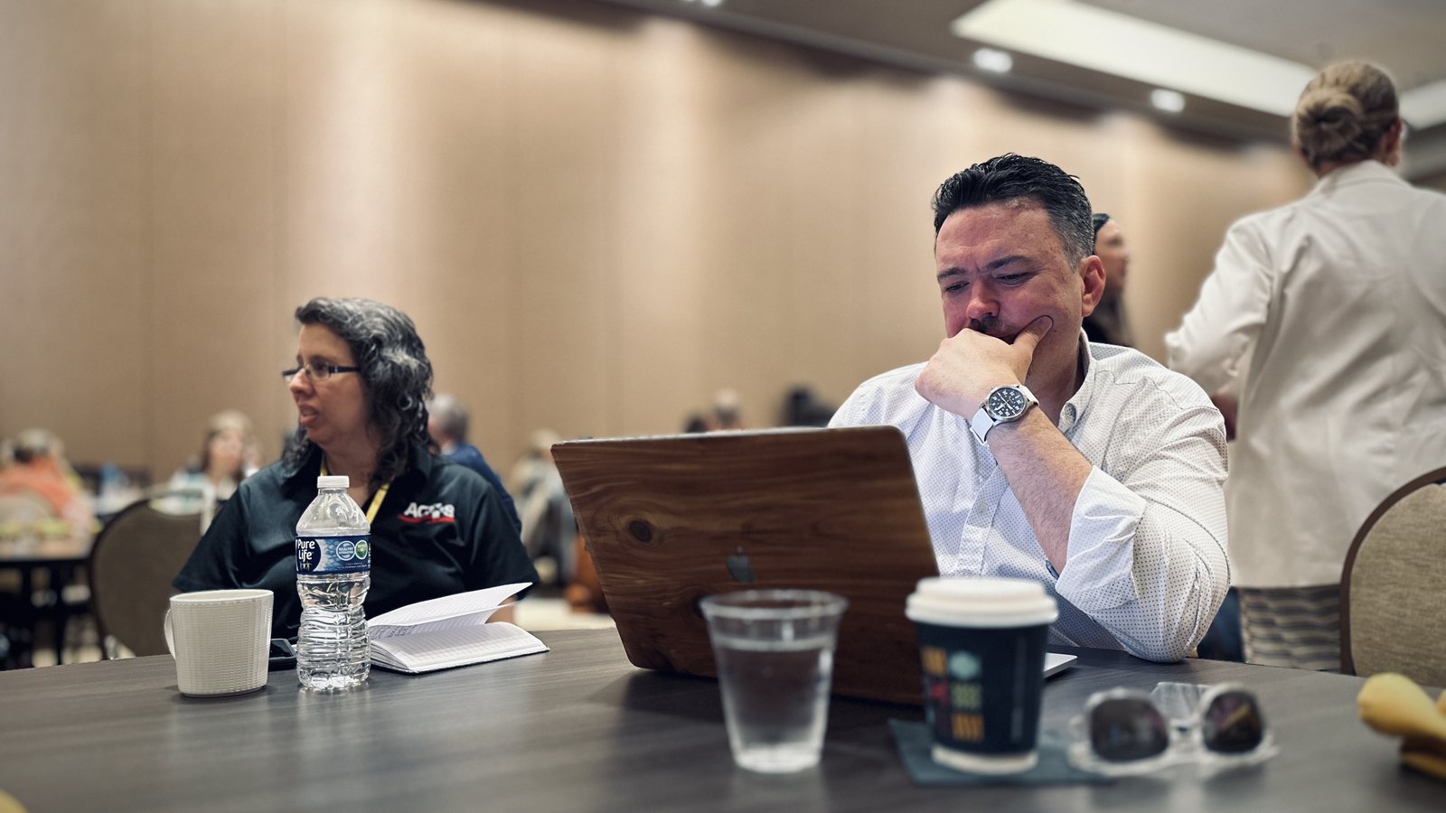 Two people working at a table, one of them looking at a laptop