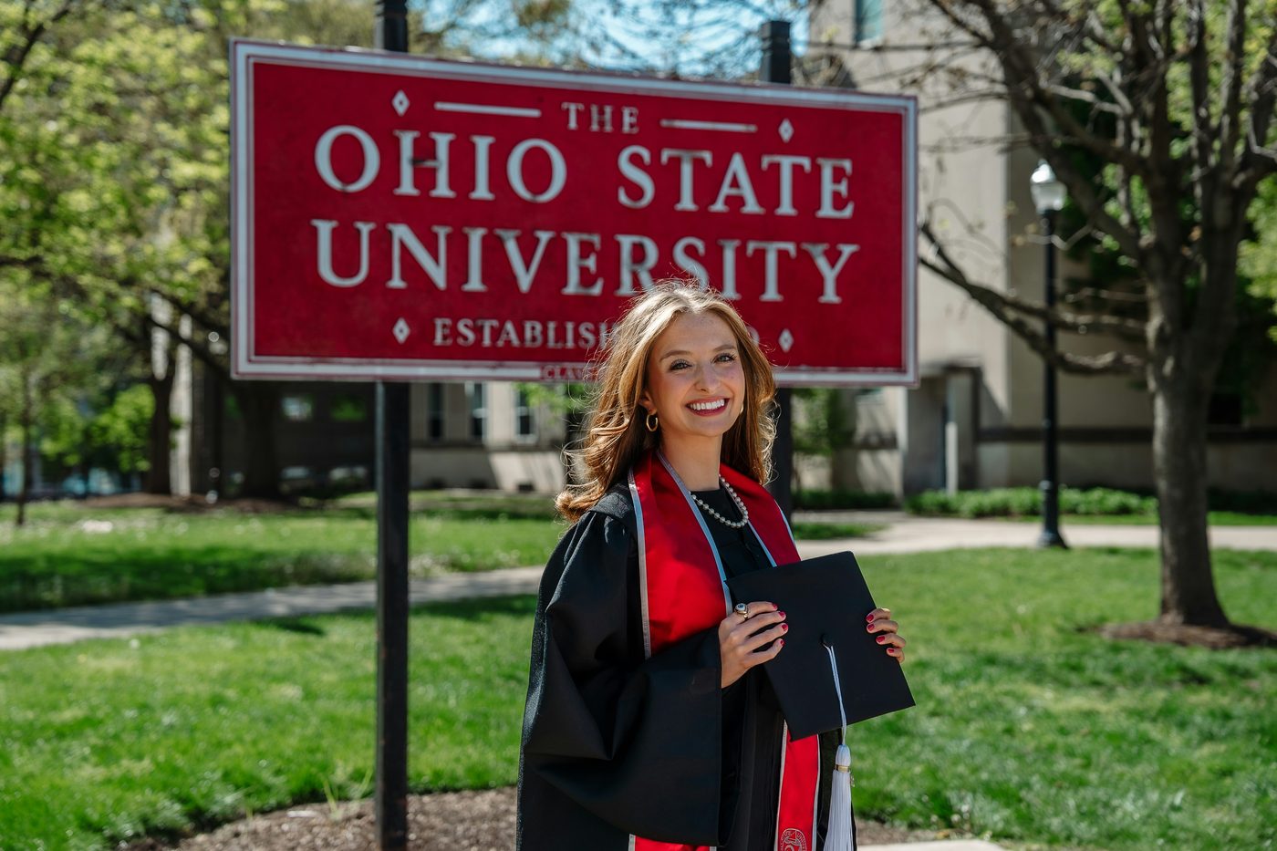 A graduate in cap and gown before The Ohio State University sign